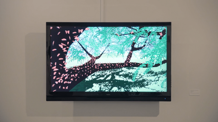 A digital animation of 300 butterflies resting on a tree branch and trunk is displayed on a screen hung on a gallery wall. A person walks in front of the screen, the movement causes the butterflies to take flight.